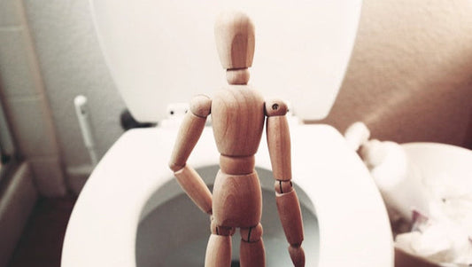 Wooden figure in front of toilet representing male discomfort, urinary irritation, or possible UTI from latex condoms.